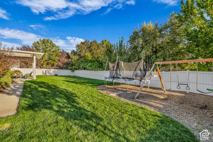 Expansive backyard featuring a lush lawn, white privacy fence, mature trees, and a paved patio with a pergola