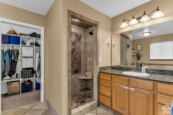 Tiled walk-in shower with a built-in bench, wood vanity with a single basin sink, and a large mirror with a four-light fixture