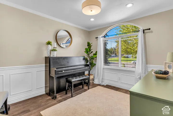 Arched picture window with blinds, recessed lighting, crown molding, and wainscoting details, complemented by wood-finish flooring