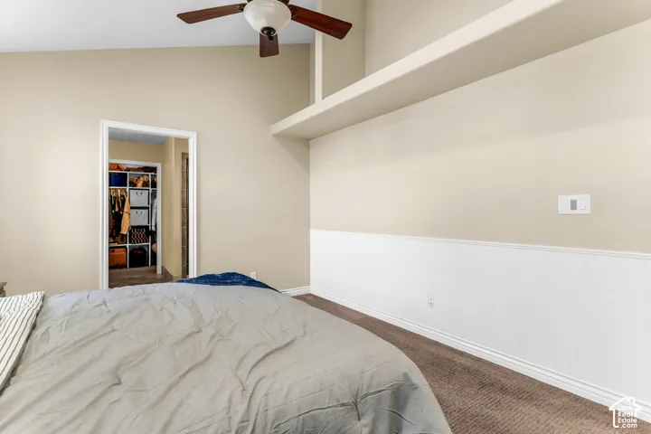 Vaulted ceiling with a ceiling fan, accent wall with wainscoting, and carpet flooring