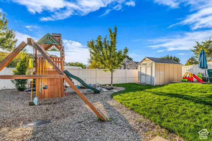 Expansive backyard featuring a manicured lawn, gravel play area, privacy fencing, and a storage shed