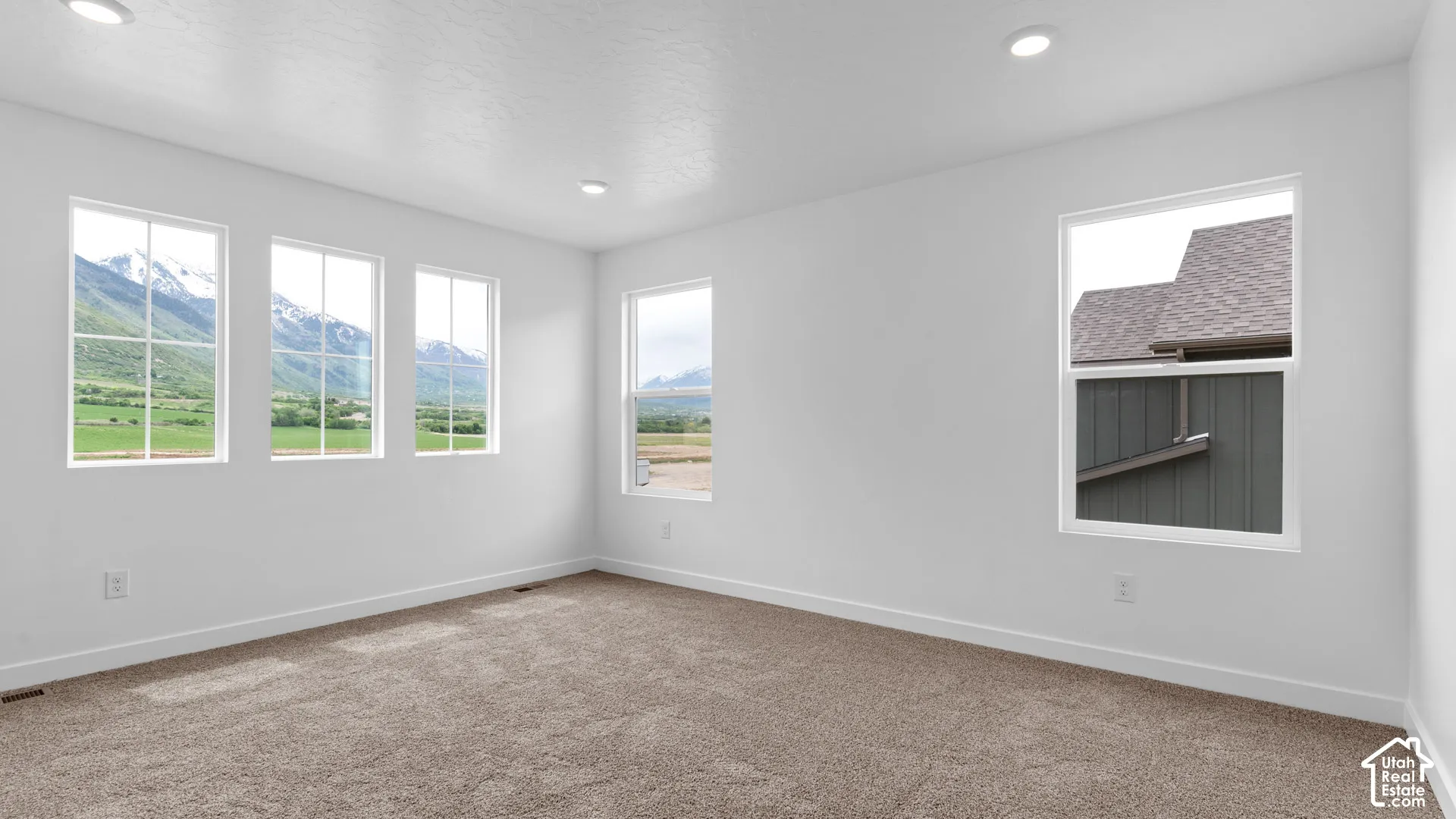 Recessed lighting, white walls, light brown carpeting, multiple windows, and mountain scenery