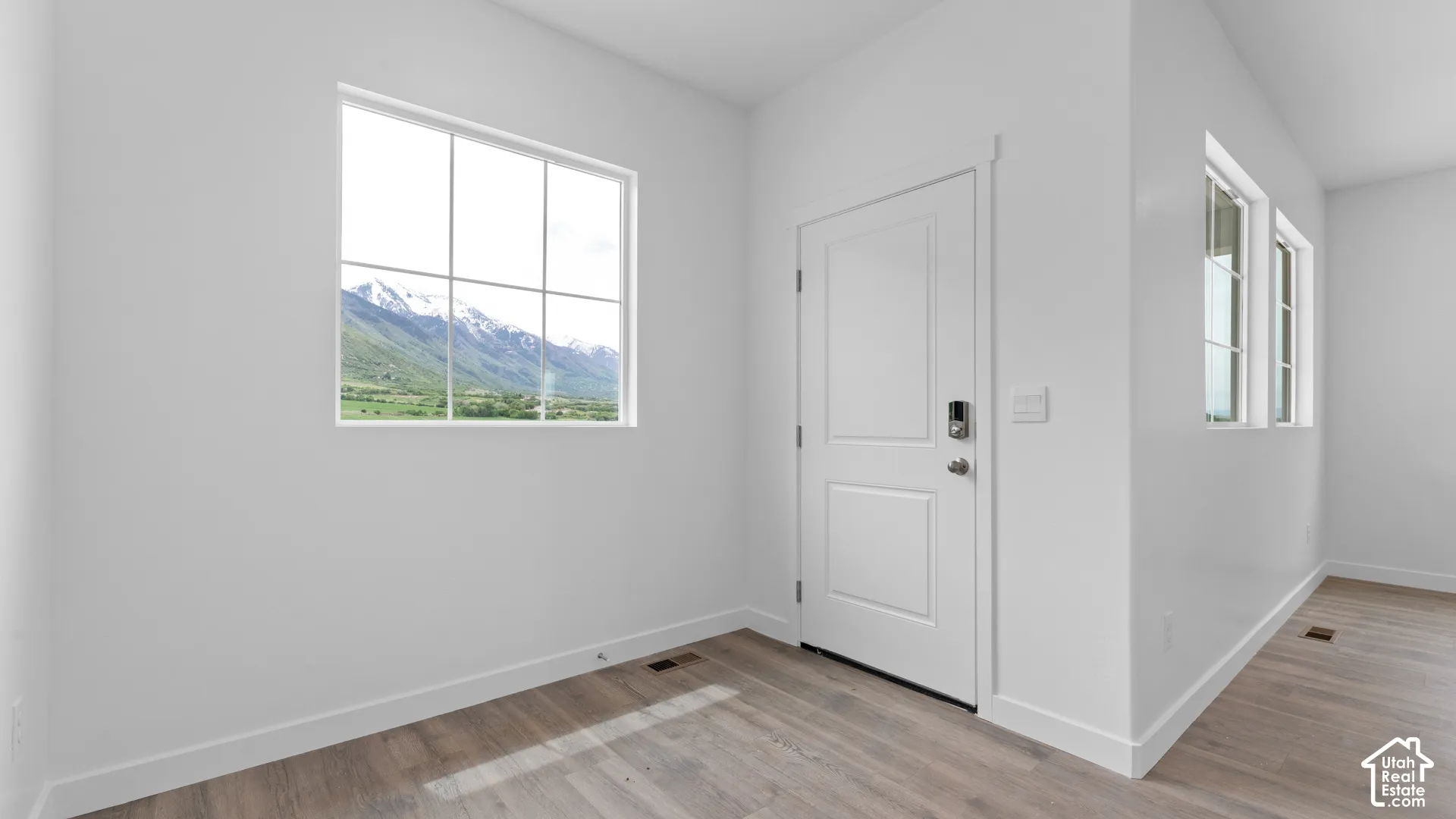 Mountain scenery through a large window, light wood-finish flooring, white walls, white trim, and a white paneled door with a keyless entry system