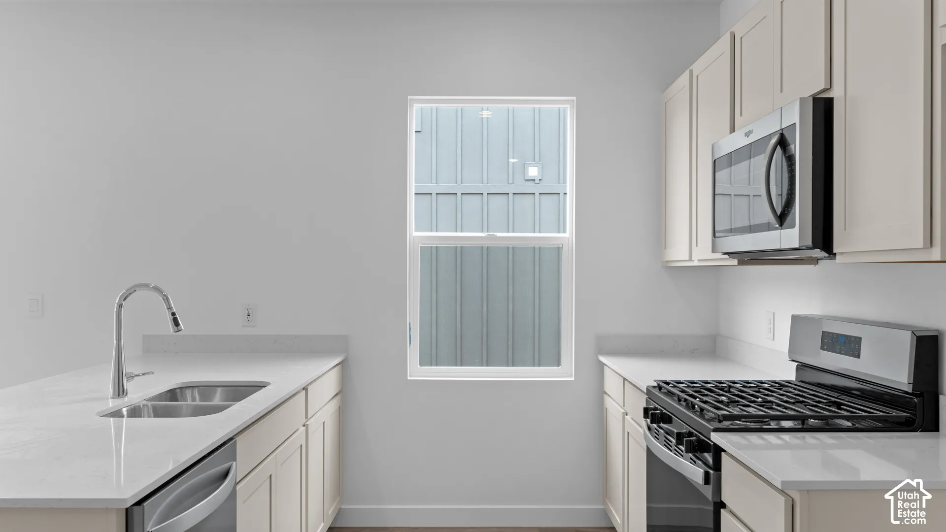 Kitchen featuring light-toned cabinetry, stainless steel appliances, a double basin sink with a gooseneck faucet, and light-colored countertops
