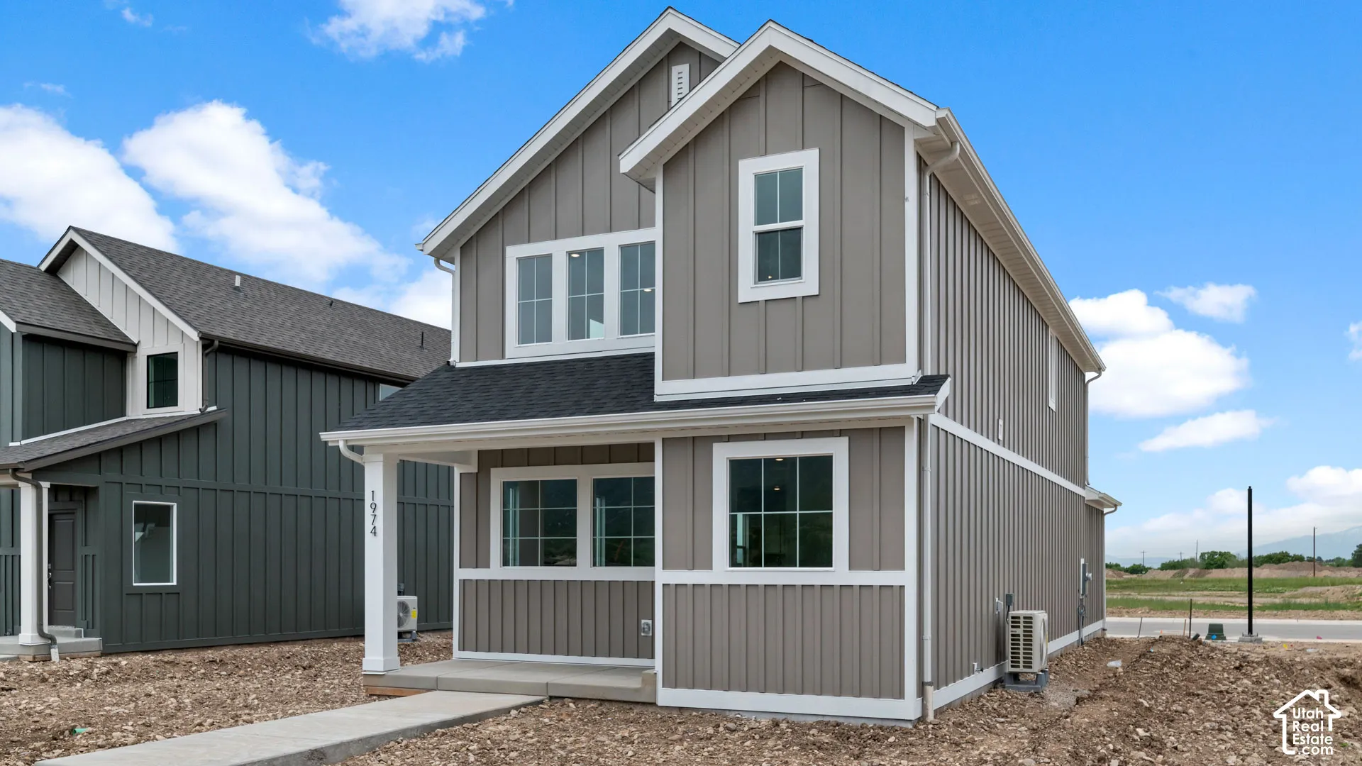 Contemporary two-story residence featuring board and batten siding, a covered entry porch with white columns, and a dark shingle roof