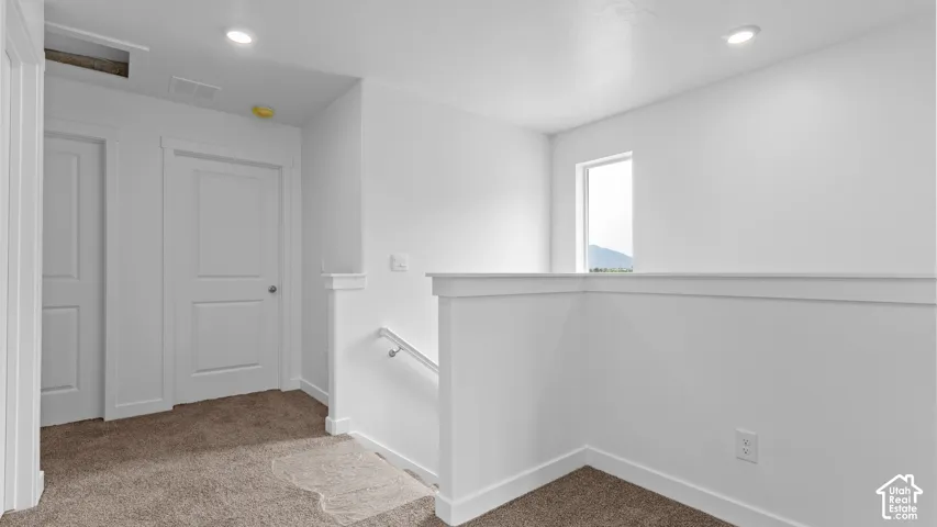 Neutral color palette with textured carpeting, recessed lighting, white trim, and a contemporary railing