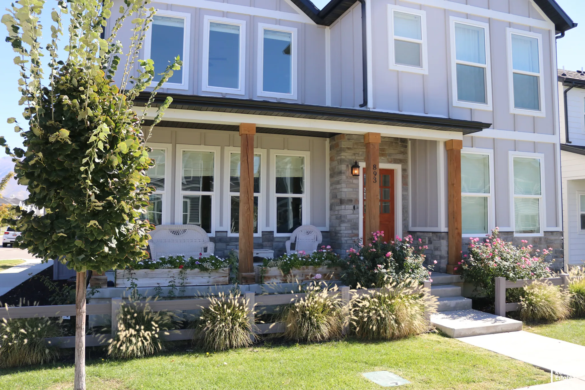 Exterior featuring board and batten siding, stone accents, a covered front porch with substantial wood pillars, and a vibrant entry door