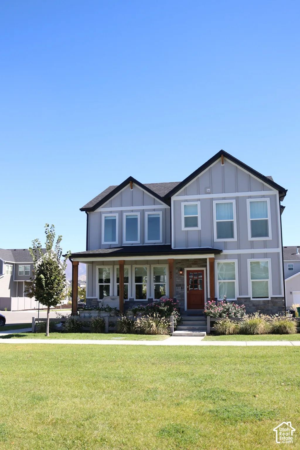 Two-story residence featuring light gray siding, dark trim, and a covered porch with natural wood posts