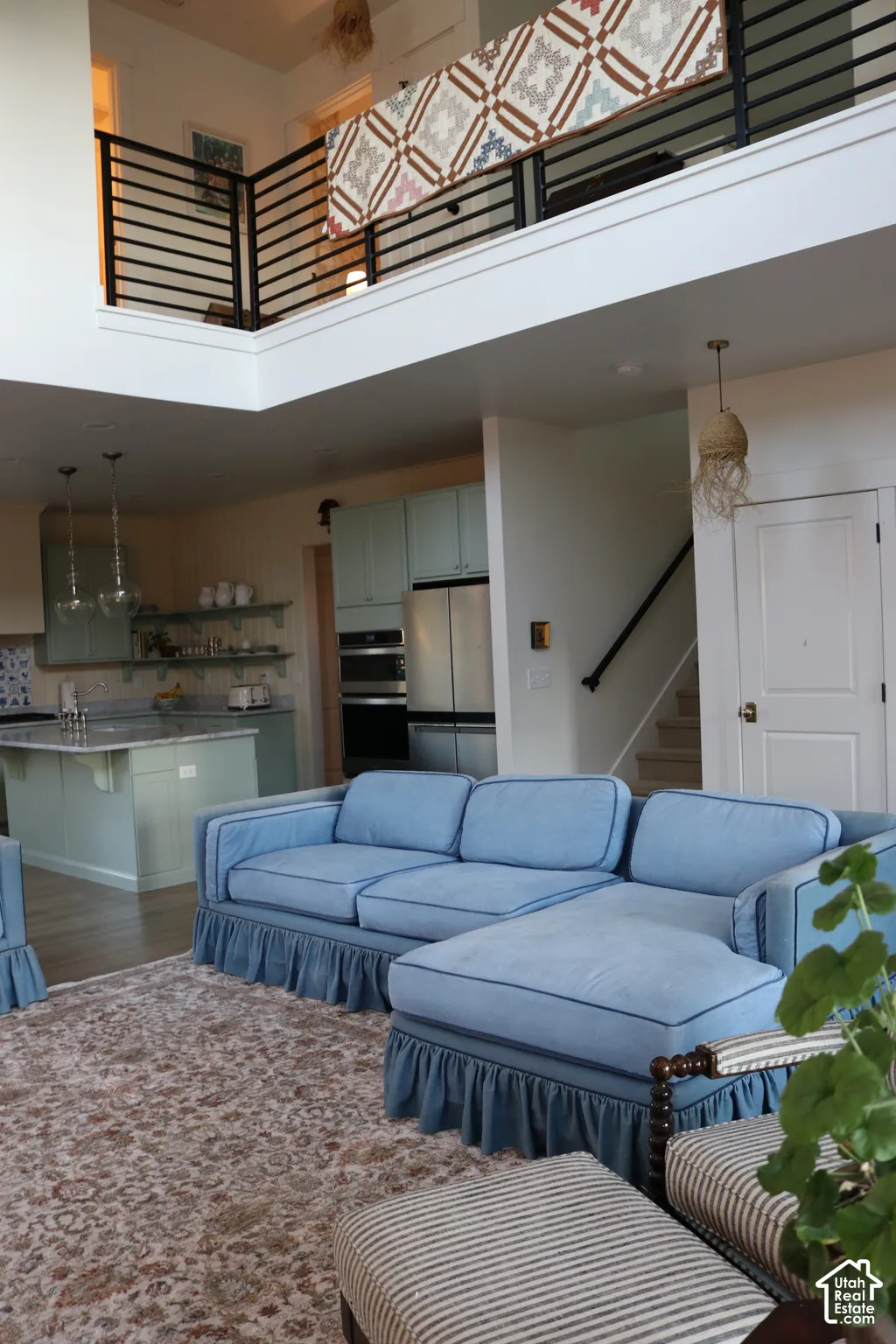 Open-concept living area with a double-height ceiling, kitchen island, stainless steel appliances, and wood-finish flooring