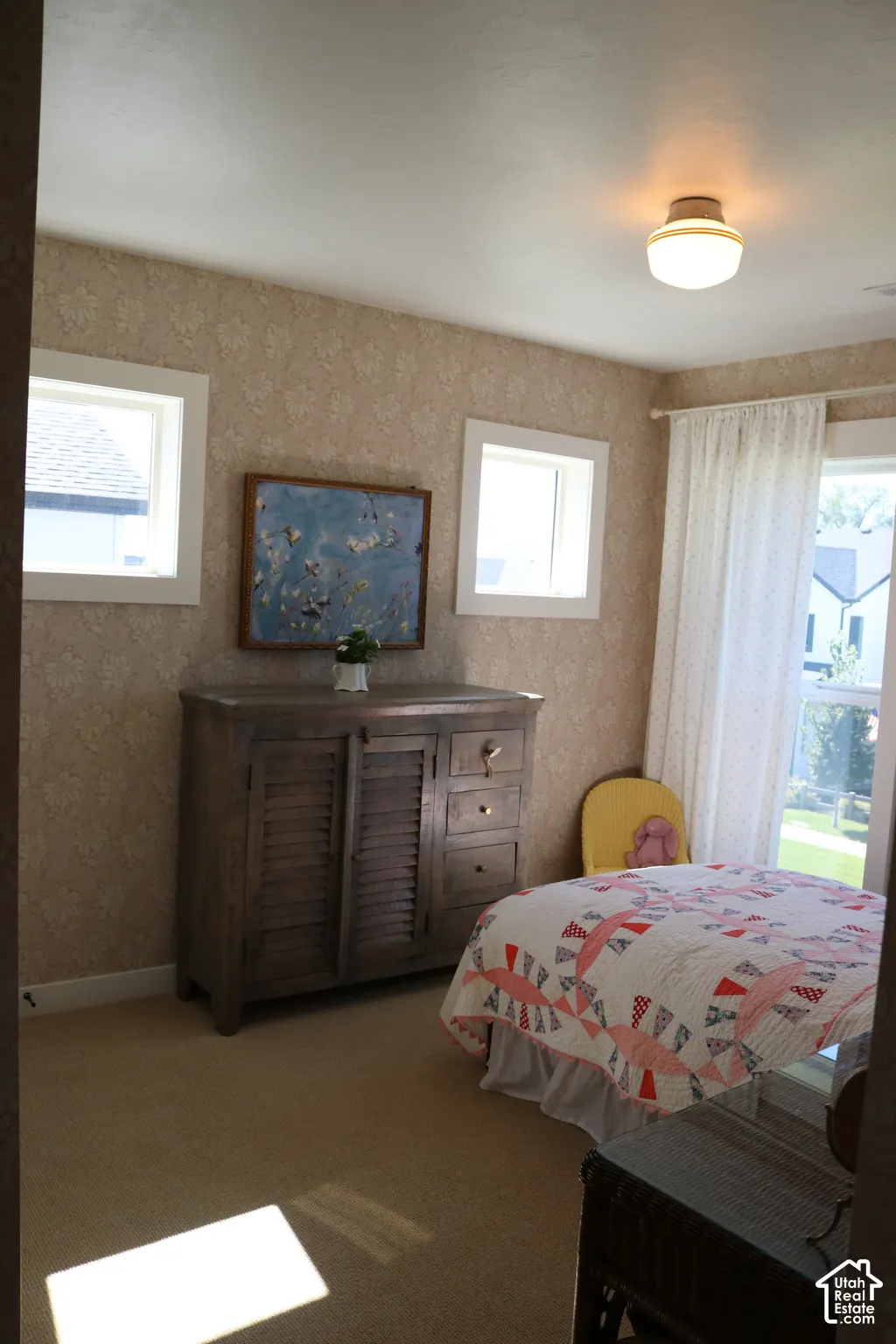 Textured wall covering, neutral carpeting, recessed windows, built-in ceiling light fixture, and a solid wood dresser