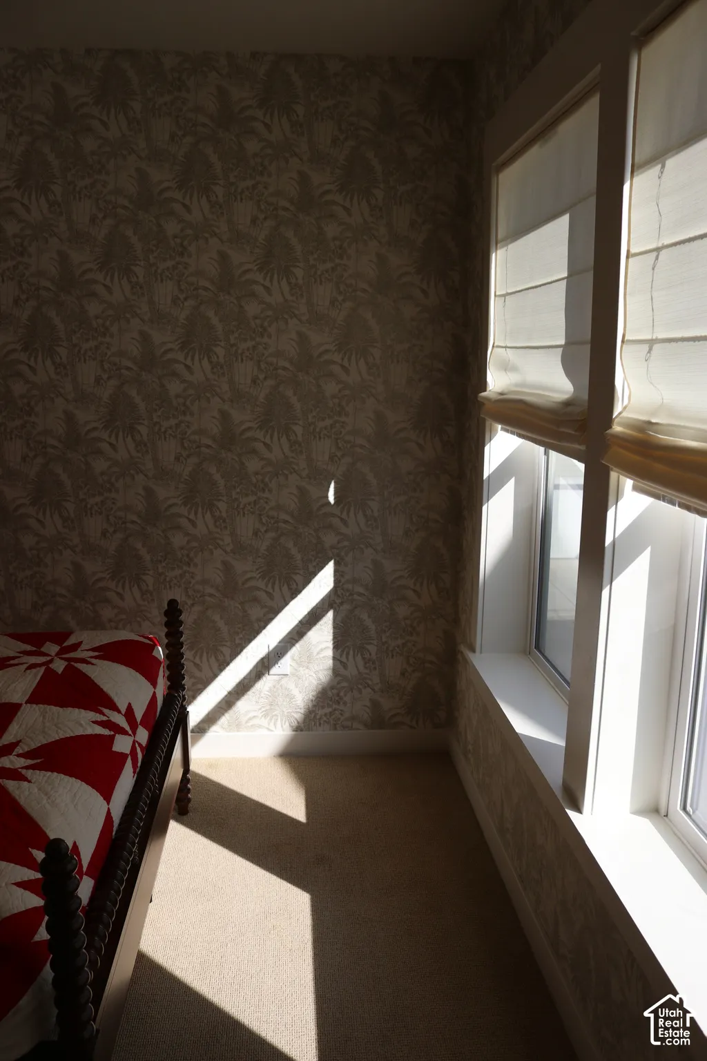 Neutral-toned carpeting, patterned wallpaper, and a window with white trim and fabric Roman shades