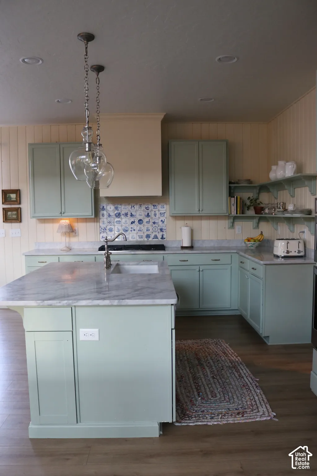 Kitchen featuring light green cabinetry, a central island with a built-in sink, stone countertops, wood-finish flooring, and recessed ceiling lighting