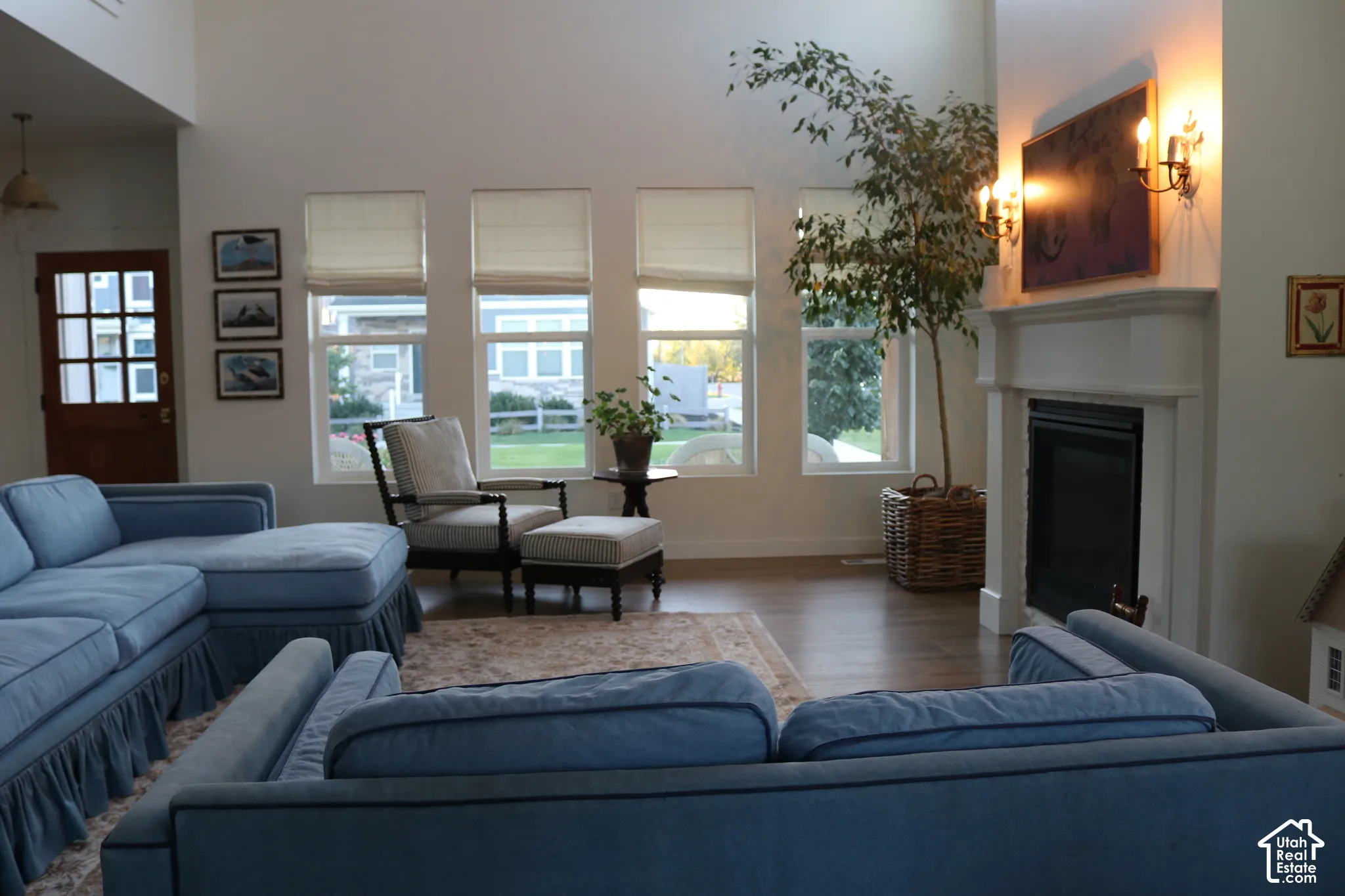 Spacious living area featuring high ceilings, wood-finish flooring, a white mantel fireplace, and multiple large windows