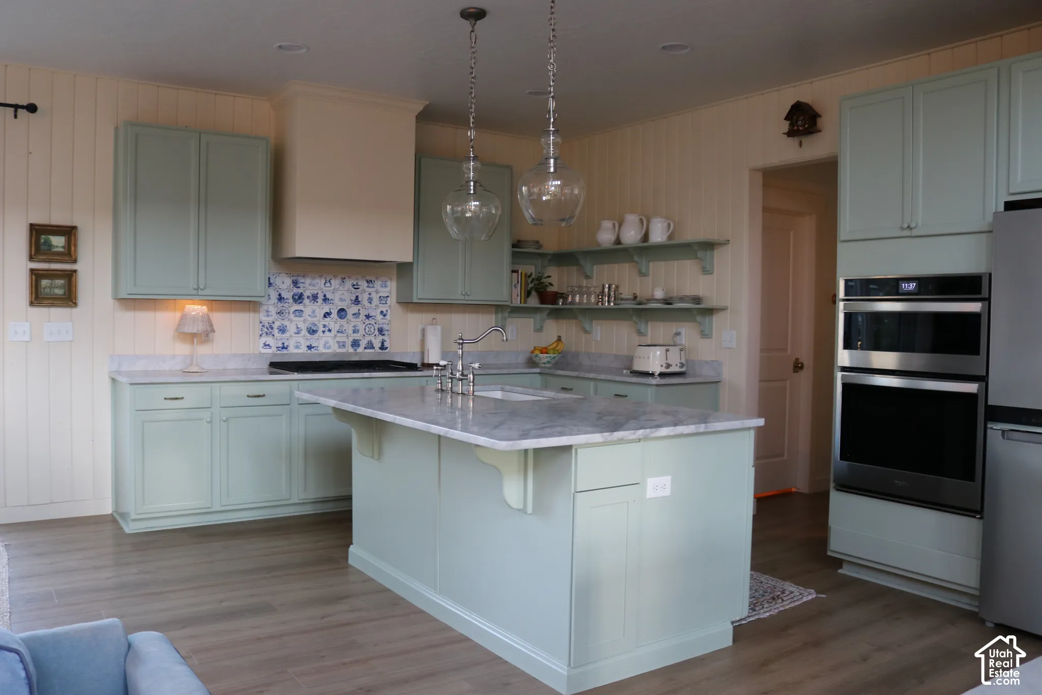 Kitchen featuring light green cabinetry, a central island with a solid surface countertop, stainless steel double ovens, and wood-finish flooring
