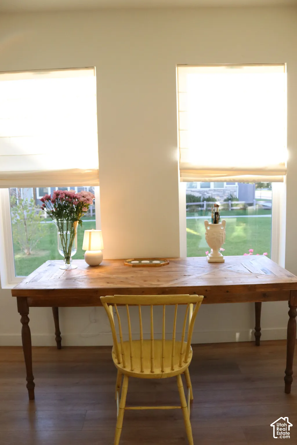 Two large windows with privacy shades, rich wood-finish flooring, and light-toned walls