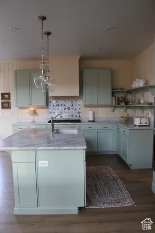 Kitchen featuring light green cabinetry, a central island with a built-in sink, stone countertops, wood-finish flooring, and recessed ceiling lighting
