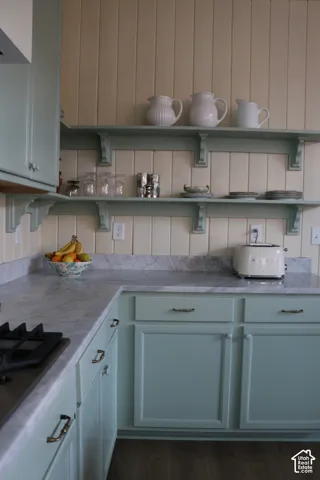 Mint green cabinetry with decorative pulls, integrated gas cooktop, light marble-finish countertops, and open shelving