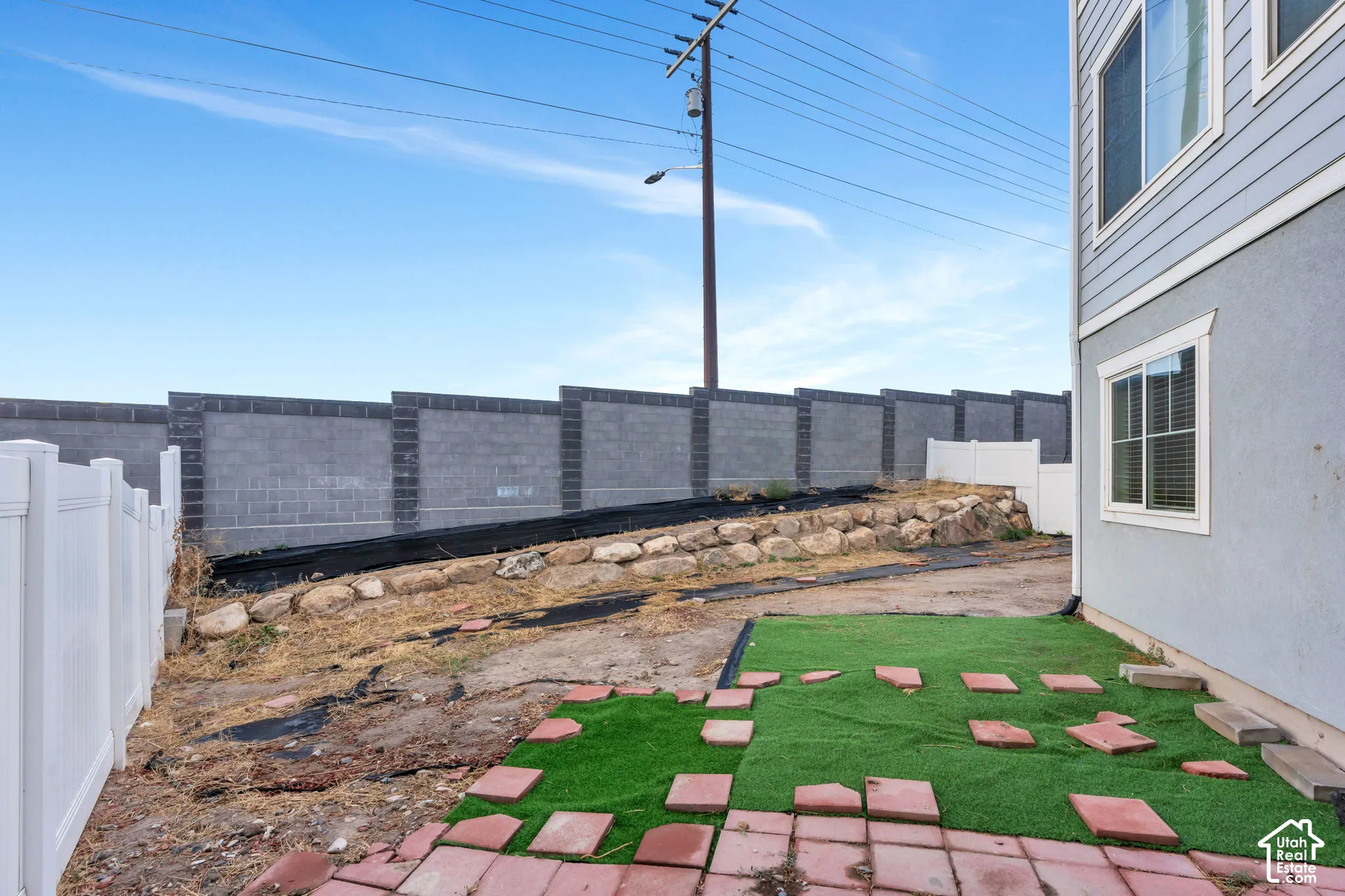 Exterior siding with white trim, multiple windows, and a partial artificial turf patch with brick pavers
