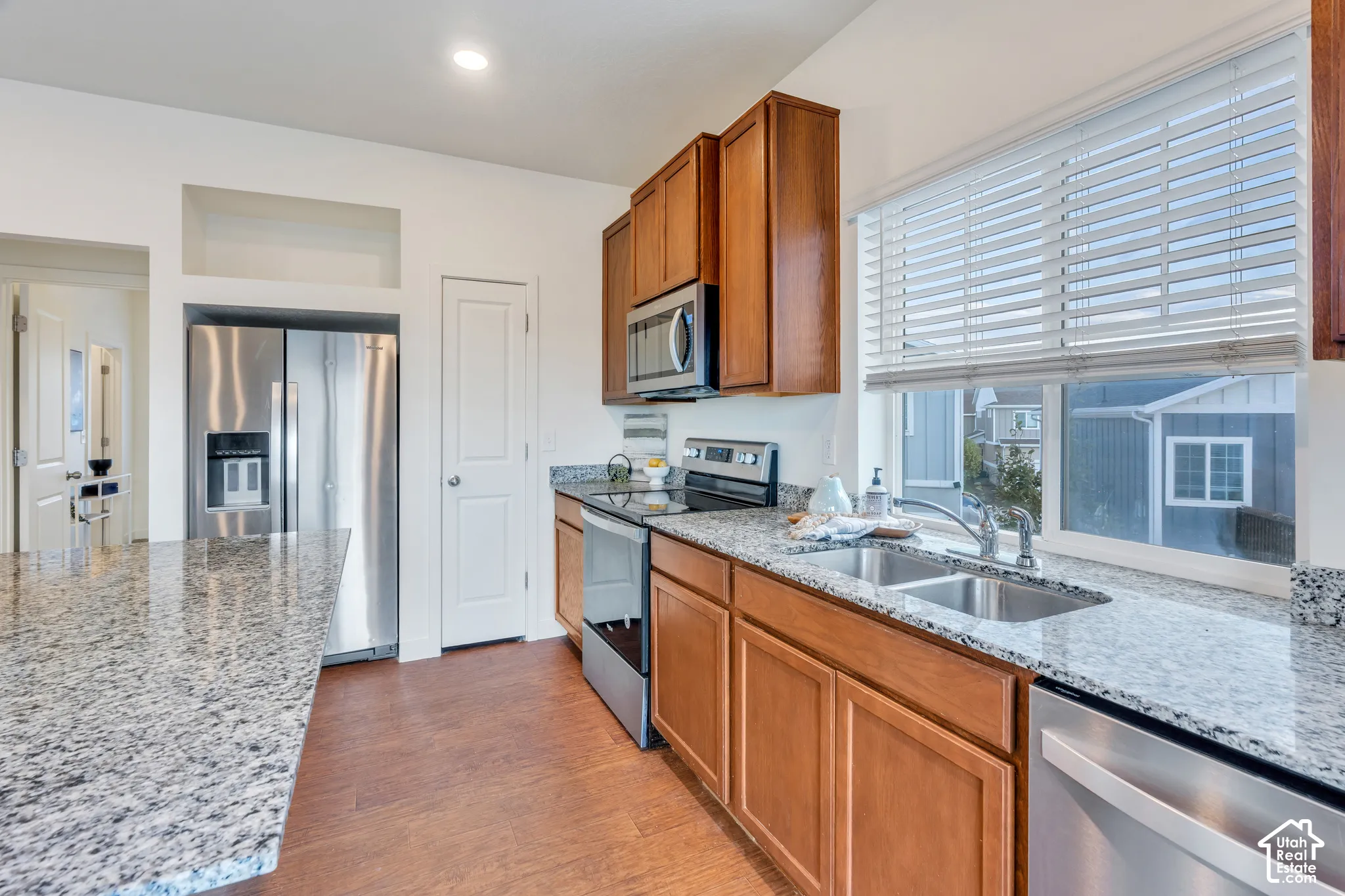 Kitchen featuring wood-finish flooring, granite countertops, wood cabinetry, and stainless steel appliances