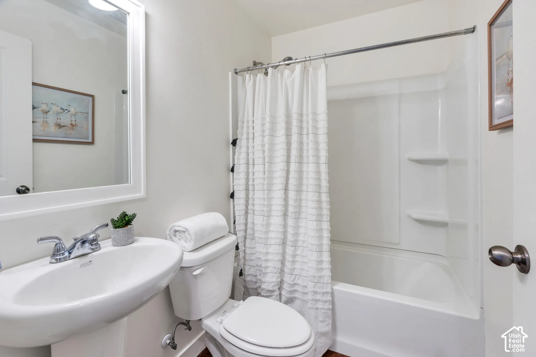 Pedestal sink with chrome faucet, white toilet, white framed mirror, and a white tub/shower combination with integrated shelving