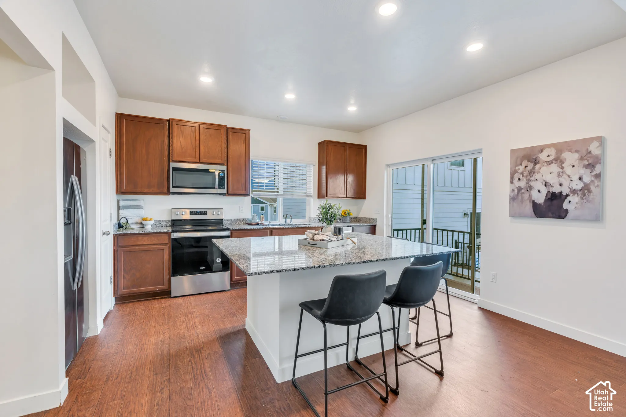 Kitchen featuring wood-finish flooring, recessed lighting, wood cabinetry, stainless steel appliances, and a kitchen island with stone countertops