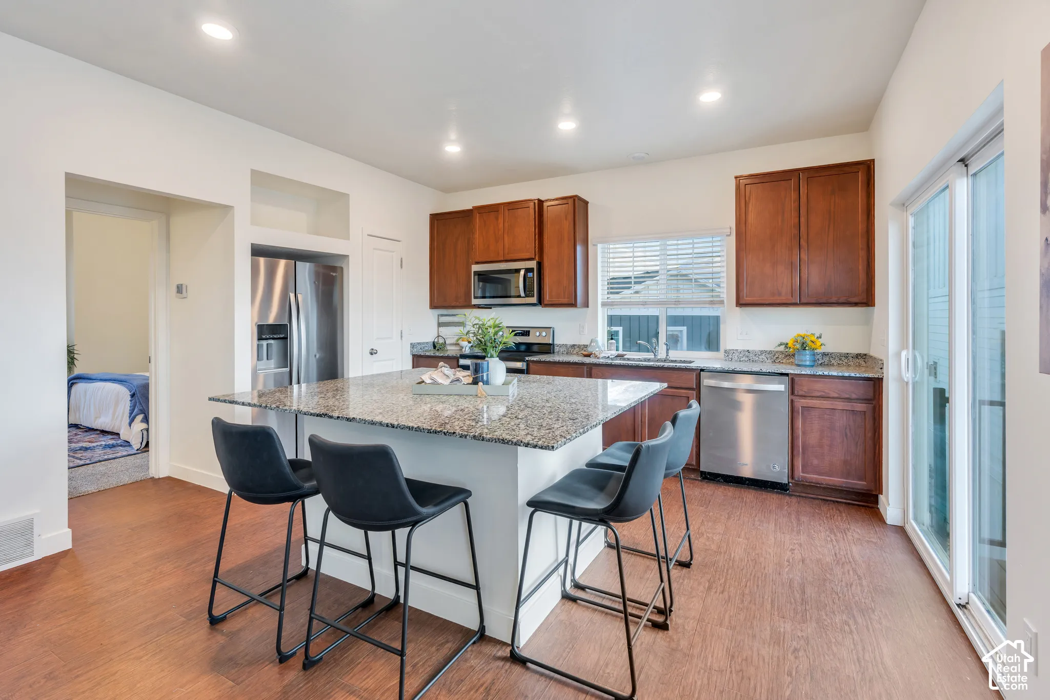 Kitchen featuring a central island with a speckled countertop, rich wood-tone cabinetry, stainless steel appliances, and wood-finish flooring