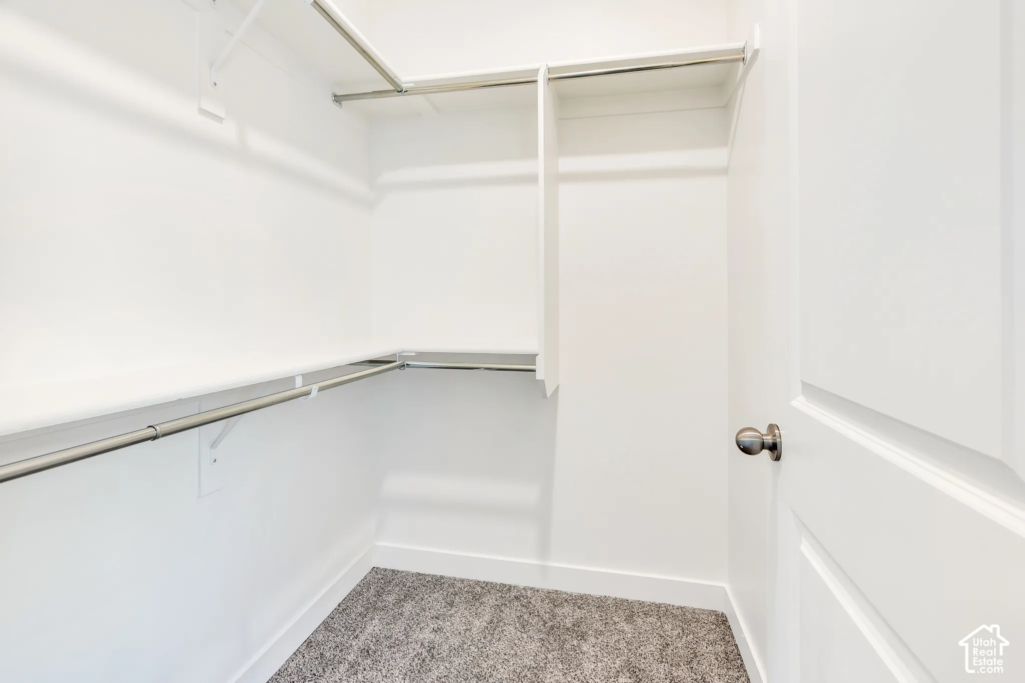 Spacious closet featuring white walls, gray carpet, and ample shelving with hanging rods