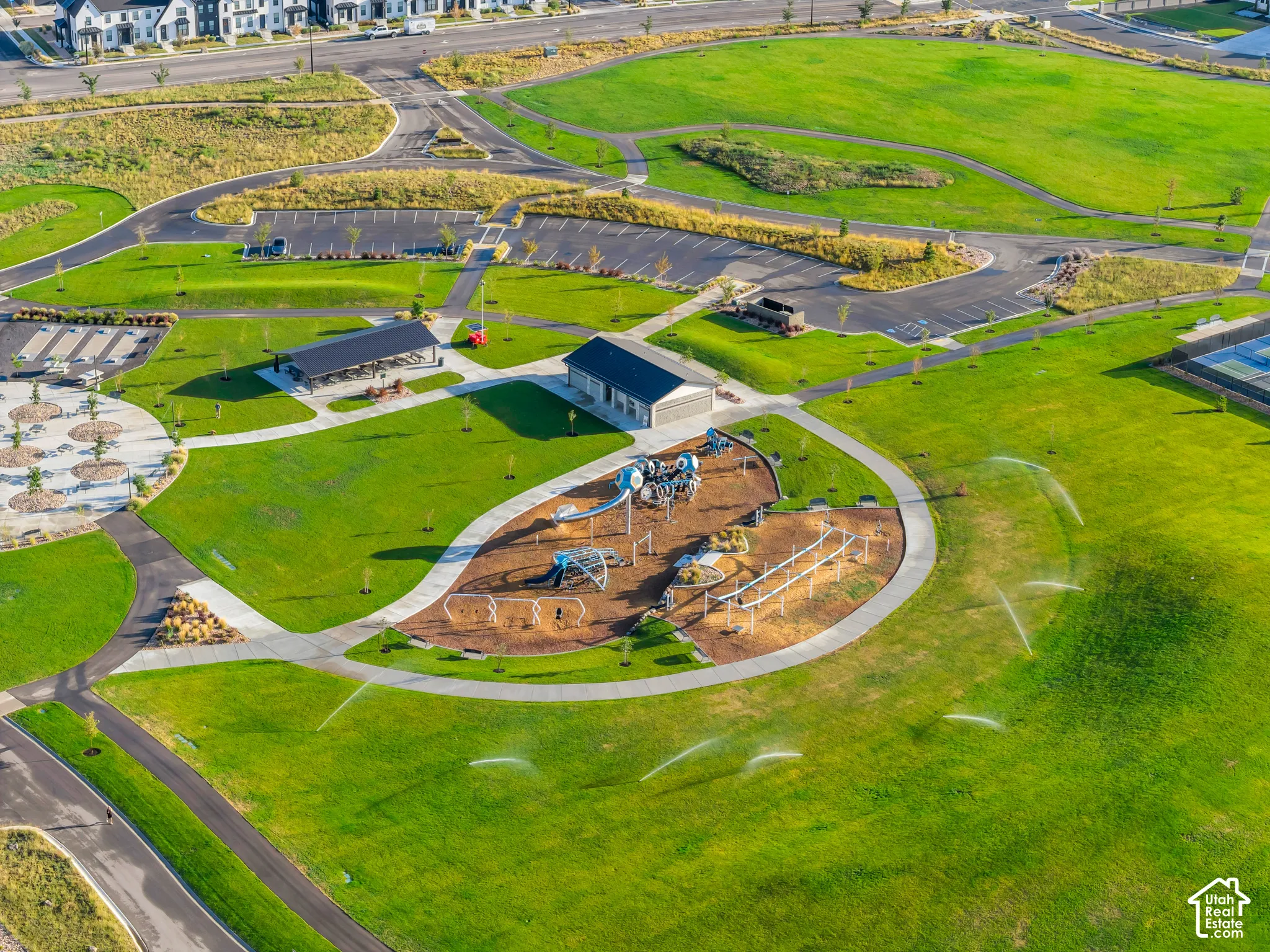 Expansive green space featuring a playground, paved pathways, a covered pavilion, and a recreation building