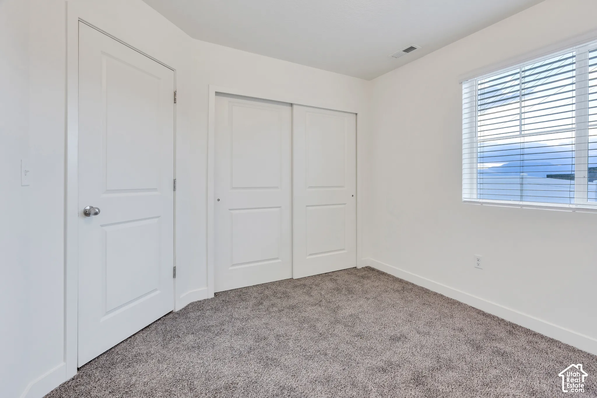 Carpeted flooring, white interior walls, white paneled doors, sliding closet doors, and a window with blinds