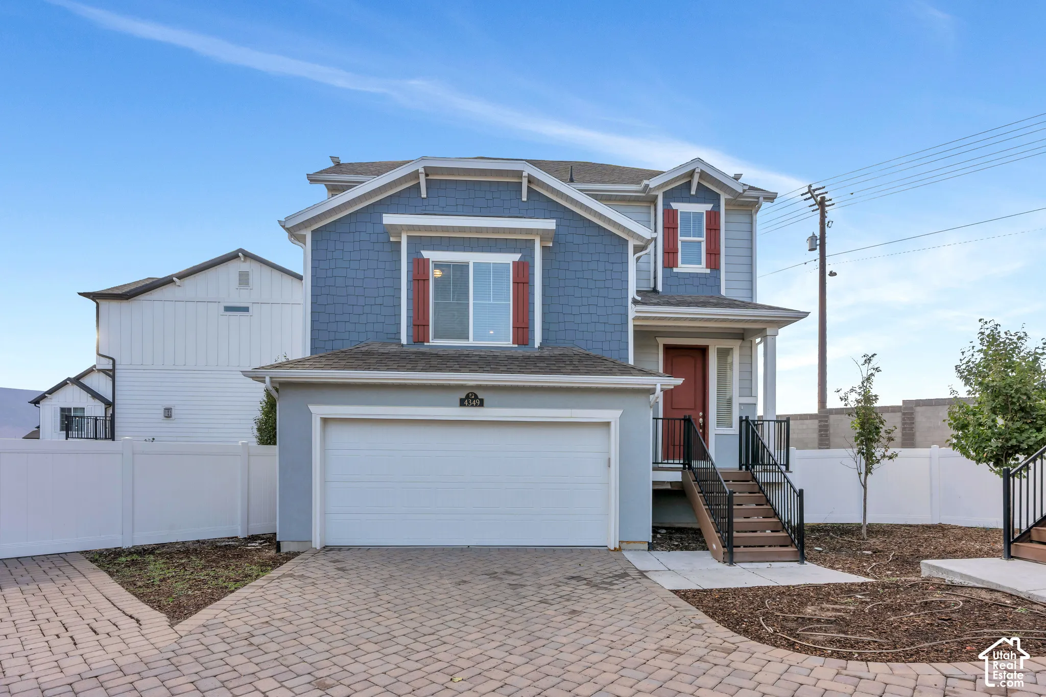 Two-story property featuring a front-facing garage, brick paver driveway, blue siding, red entry door, and exterior stairs with black railings