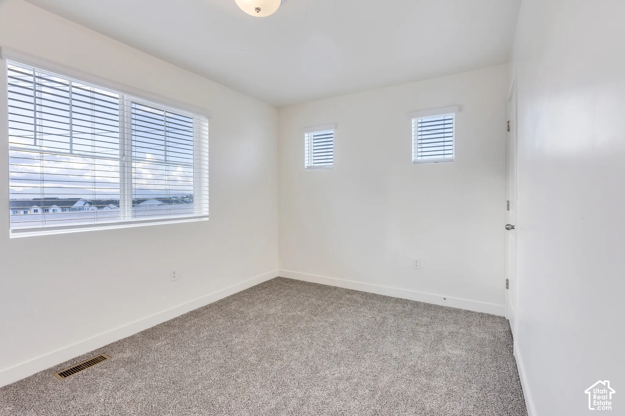 Plush carpeting, bright white walls, multiple windows with blinds, and a flush mount ceiling light fixture