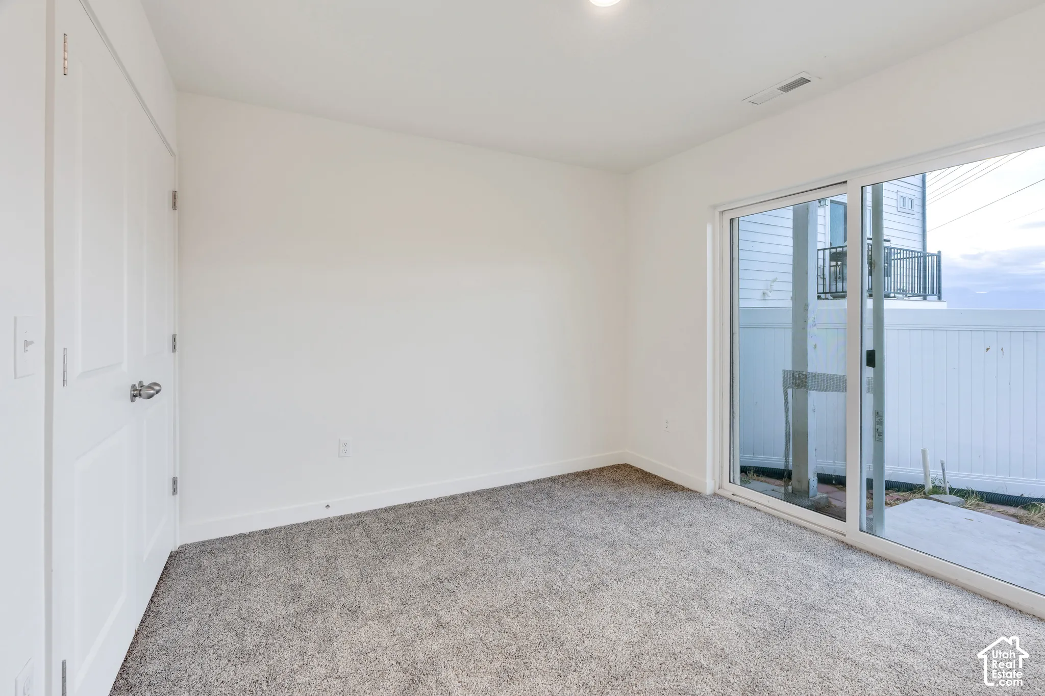 Sliding glass door, wall-to-wall carpeting, overhead lighting, white walls, and a private exterior patio