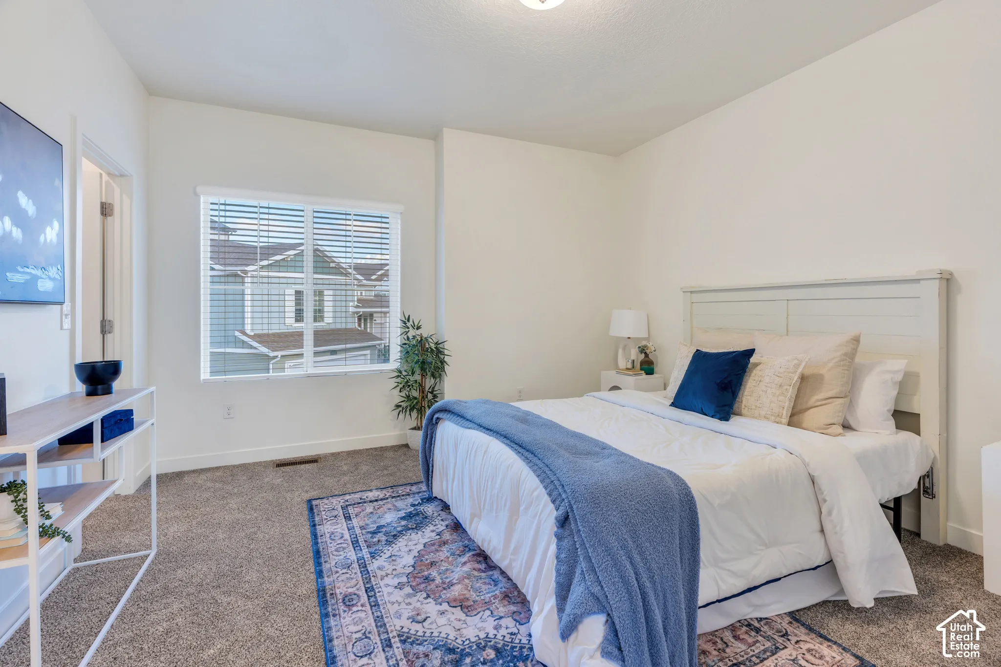 Bright white wall finishes, neutral carpeting, and a large window with blinds