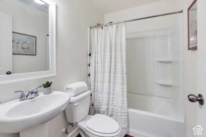 Pedestal sink with chrome faucet, white toilet, white framed mirror, and a white tub/shower combination with integrated shelving