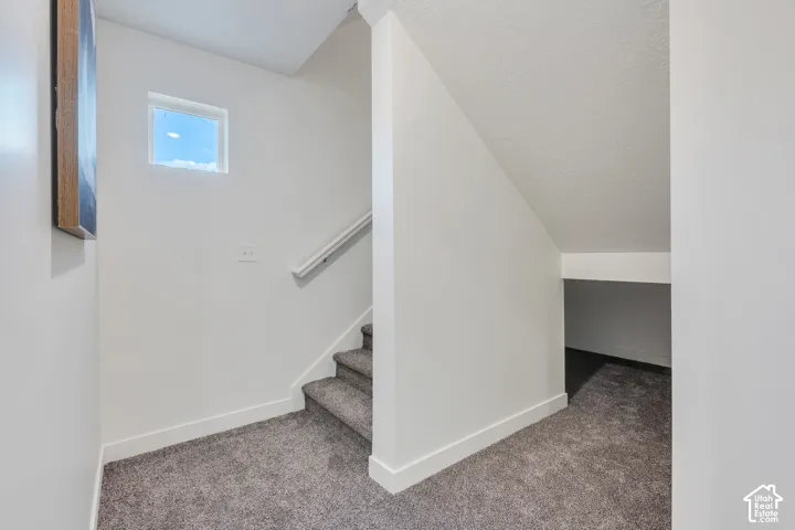 Carpeted staircase with wall-mounted handrail, leading to a landing with a square window and a built-in recess