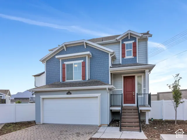 Two-story residence featuring a red front door, blue shingle siding, a front porch with dark railings, an attached garage, and a paver driveway