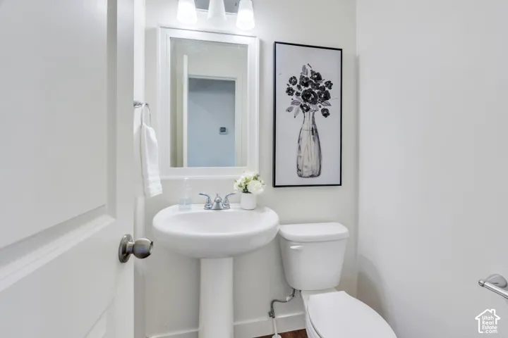 Pedestal sink with chrome faucet, white toilet, and overhead vanity lighting