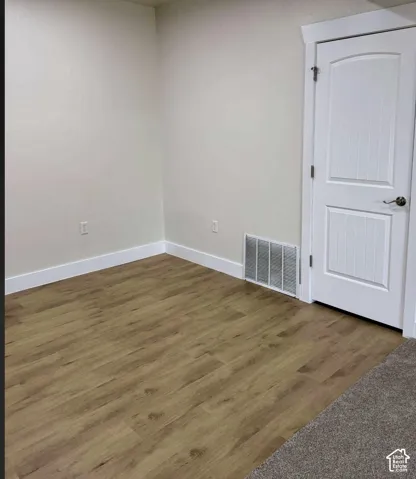 Wood-finish flooring with white trim, light neutral wall color, and a white interior door with a paneled design