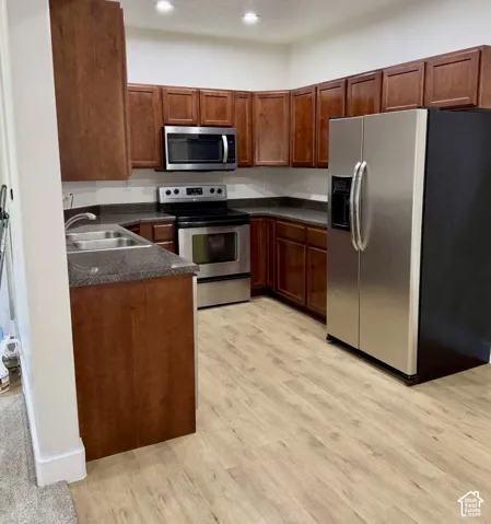 Kitchen featuring wood-finish flooring, stainless steel appliances, dark countertops, and ample brown cabinetry