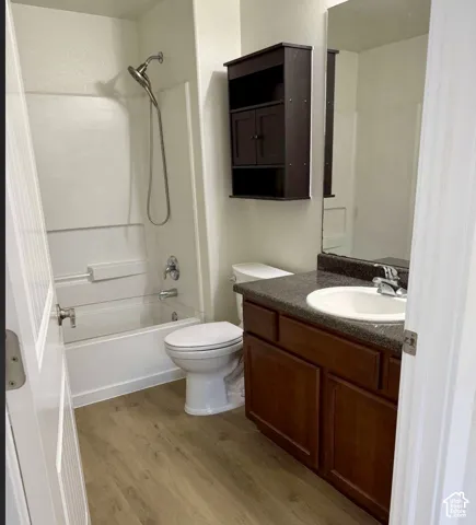 Wood-finish flooring, dark wood vanity with white basin sink, dark countertop, and shower/tub combination