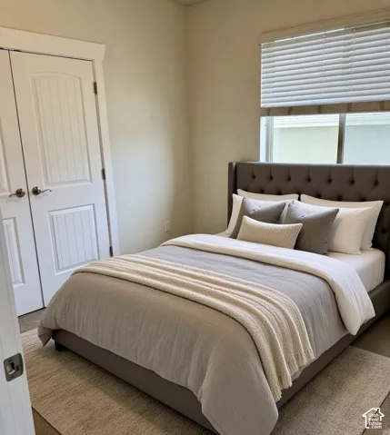 Hardwood-style flooring with a tufted upholstered headboard, white trim, and window blinds