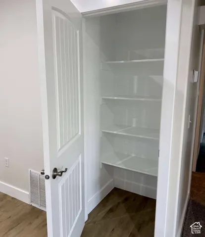 Storage closet with multiple white shelves, wood-finish flooring, and a white paneled door