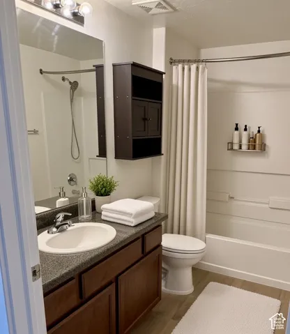 Built-in vanity with a composite countertop and integrated sink, dark wood-finish cabinetry, full-width mirror with overhead lighting, and a bathtub with a shower and curved shower rod
