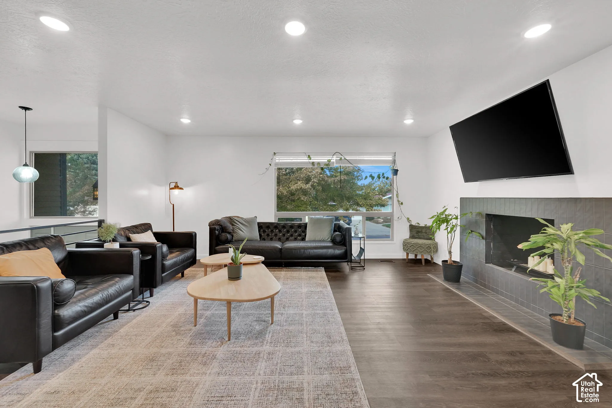 Recessed lighting, wood-finish flooring, large window, fireplace with dark tile surround, and an open-concept layout