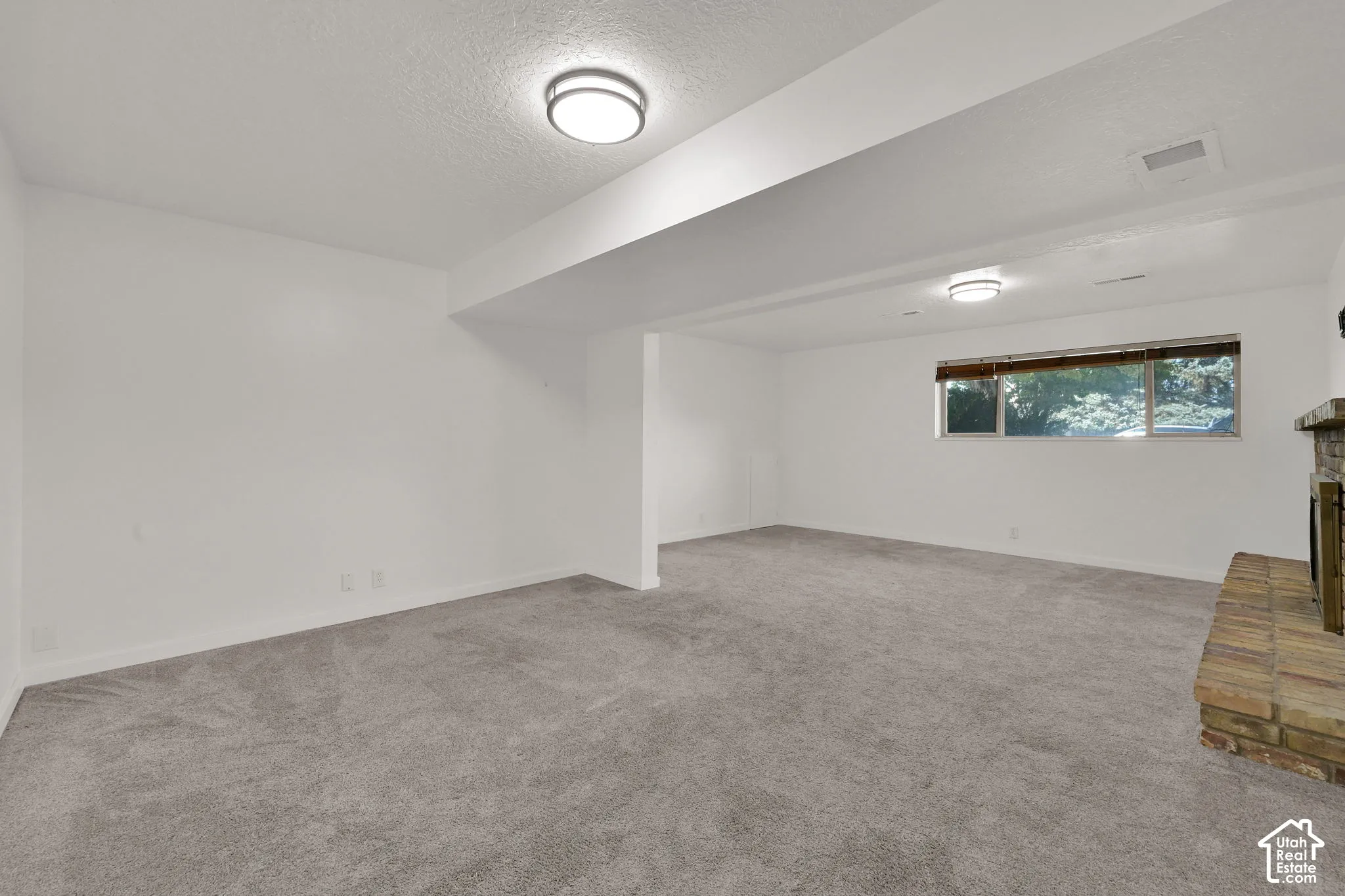 Expansive carpeted area with a brick hearth fireplace, multiple windows, and recessed lighting