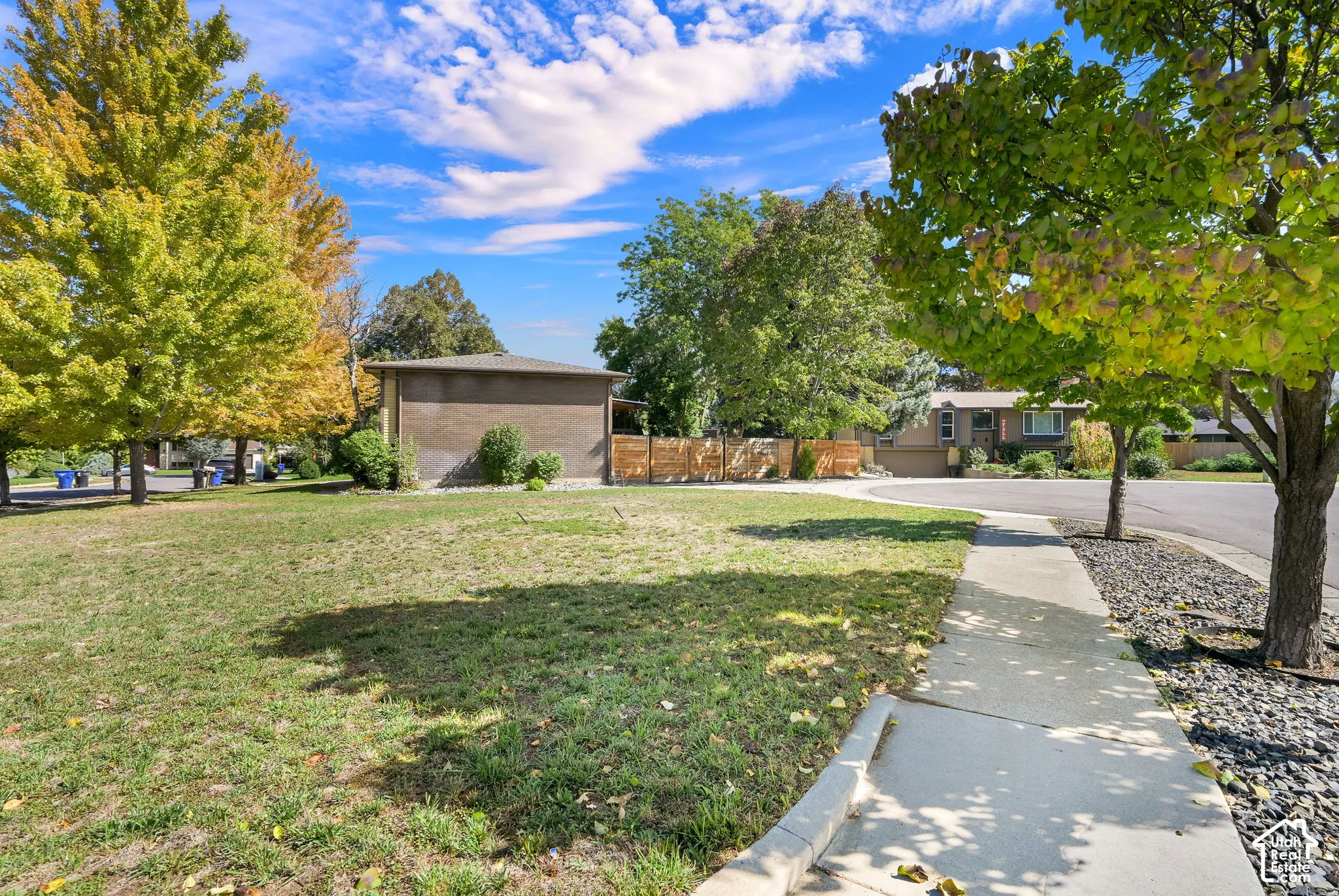 Manicured side yard with mature trees, paved sidewalk, and drip system set up