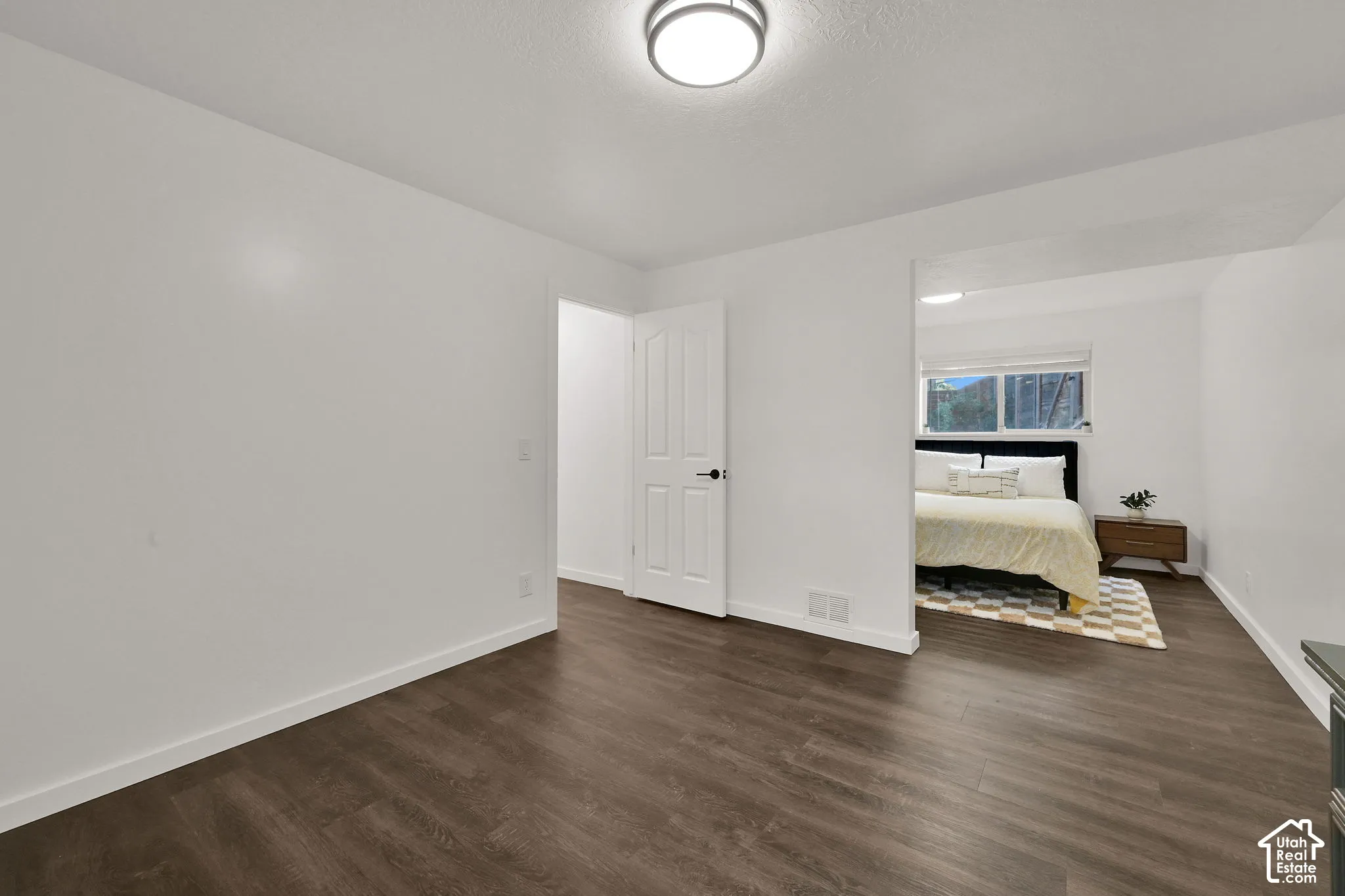 4th bedroom with wood-finish flooring throughout, white walls, flush mount ceiling light, and a white interior door with black hardware
