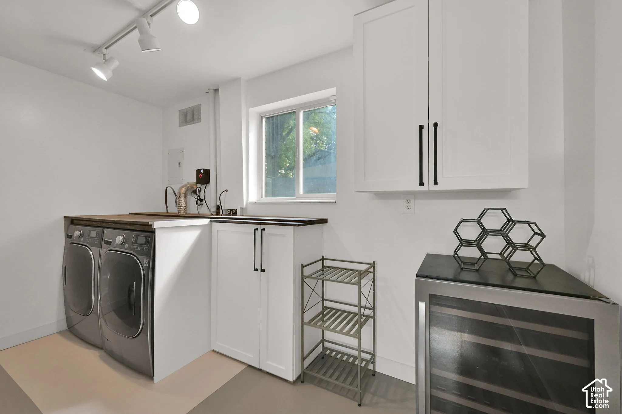 White cabinetry with black hardware, wood-finish countertop, utility sink, and track lighting