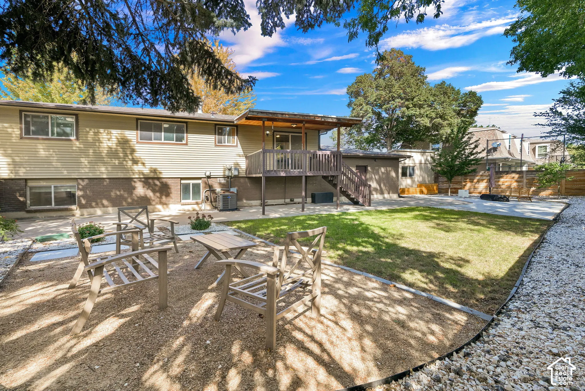 Expansive backyard featuring a manicured lawn, a raised wood deck with staircase, and a gravel patio seating area