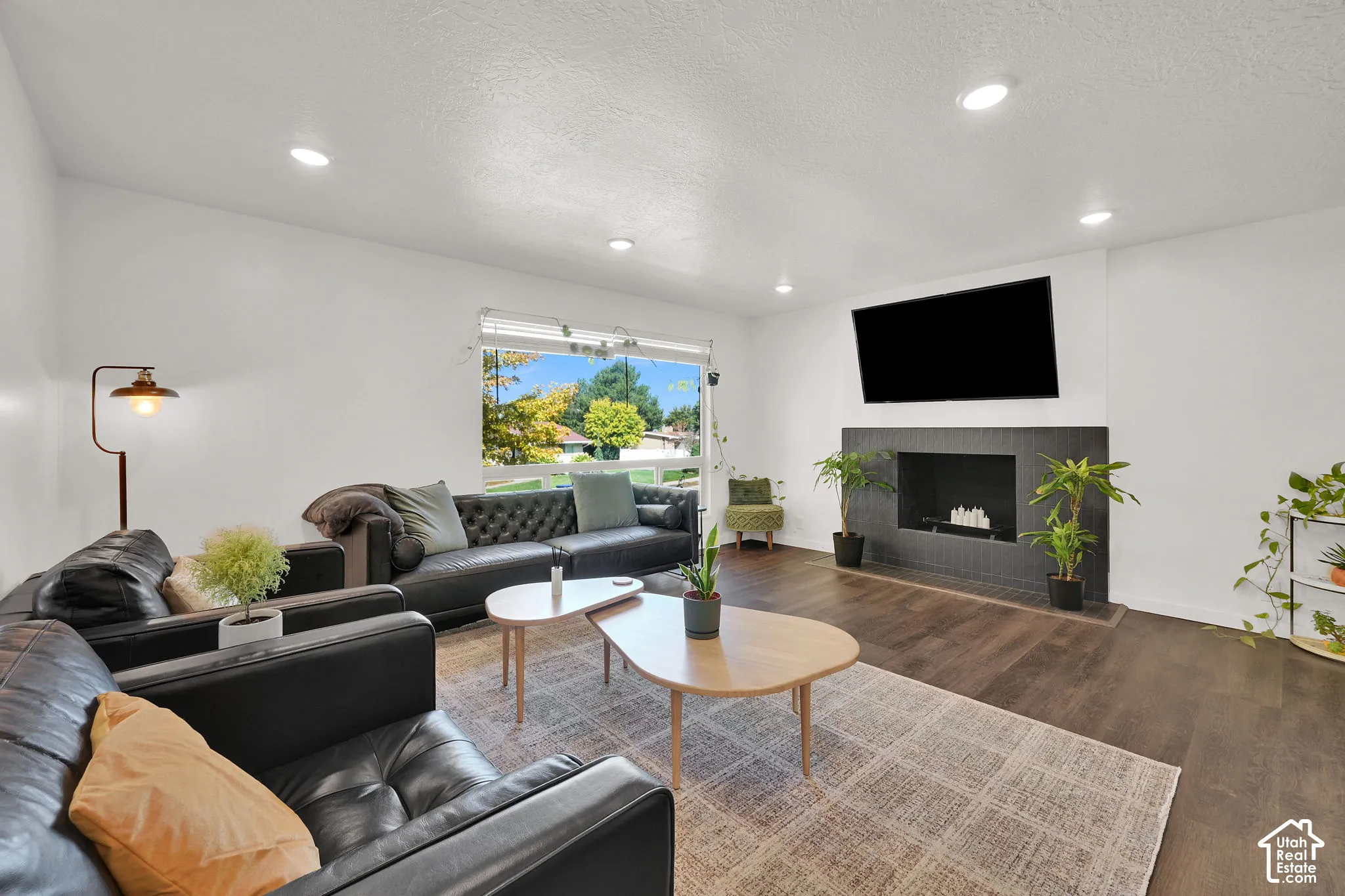 Spacious living area featuring recessed lighting, large window with outdoor scenery, modern fireplace with a dark tile surround, and wood-finish flooring